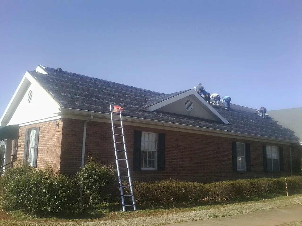 Crew tearing shingles off a brick ranch roof with a ladder set — Metal Roof Repair work by our crew in Dunn Loring
