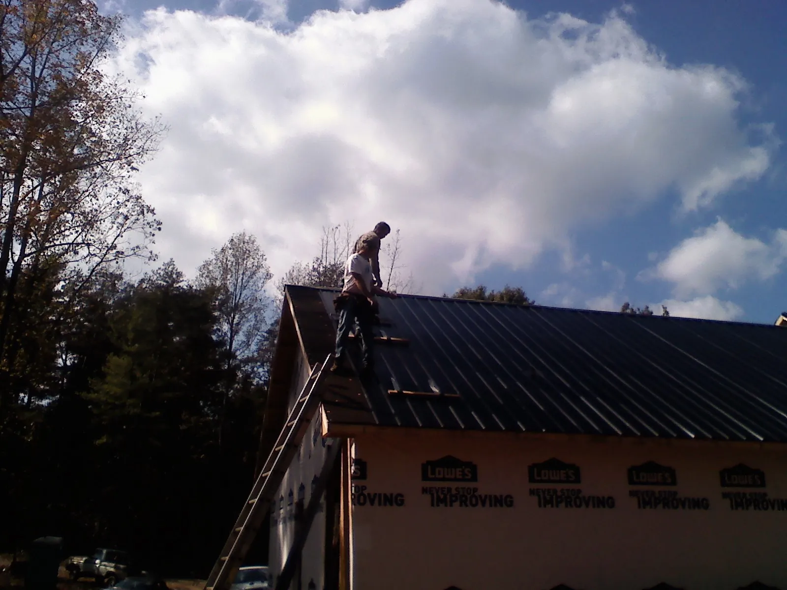 Roofer fastening dark metal panels high against a cloudy sky, from a Roof Inspection job in Dunn Loring