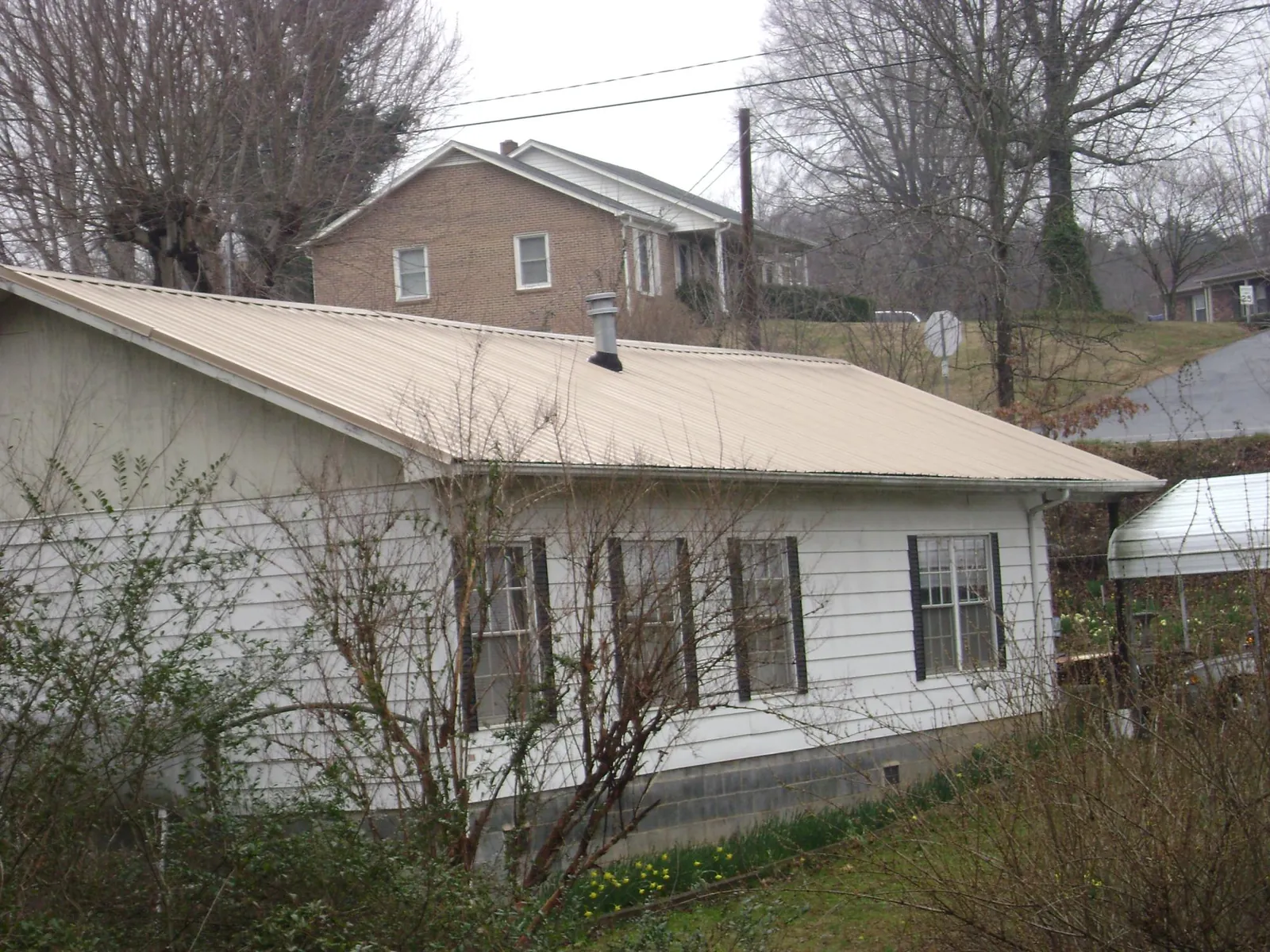 Tan metal roof on a white sided house set into a hillside — Commercial Roofing by Roofing Brothers in Dunn Loring